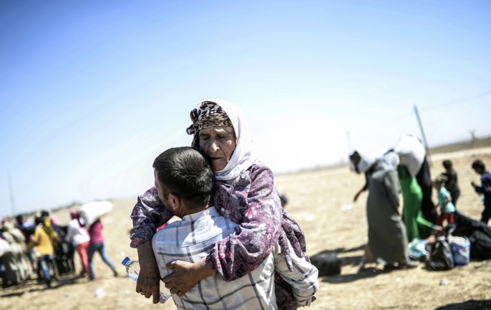 A Syrian Kurd carries an elderly woman after crossing the border between Syria and Turkey near the southeastern town of Suruc in Sanliurfa province, Turkey, on September 20, 2014. Several thousand Syrian Kurds began crossing into Turkey on September 19 fleeing Islamic State fighters who advanced into their villages, prompting warnings of massacres from Kurdish leaders. (Bülent Kılıç/AFP)