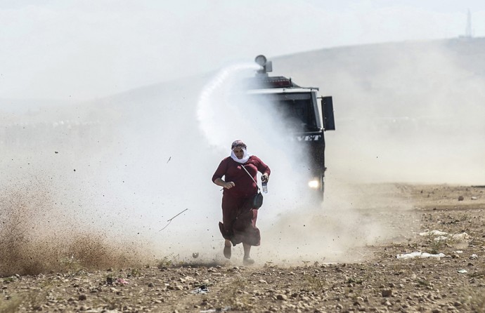 A Kurdish woman runs away from a water cannon during clashes with Turkish soldiers near the Syrian border after Turkish authorities temporarily closed the border, preventing Syrian Kurds who had accompanied their families to safety inside Turkey, from returning to the battlefront, on September 22, 2014. (Bülent Kılıç/AFP)