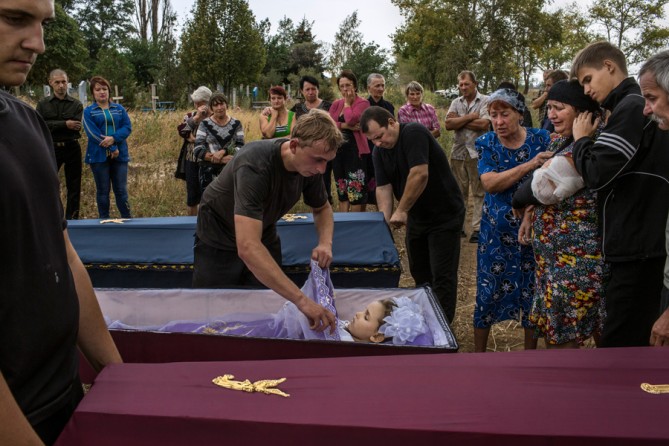 Sept. 8, 2014. A cemetery employee covers the body of 6-year-old Karolina Baykina as another closes the coffin of her brother, 10-year-old Nikita, in the small village of Lebedinskoye. Their injured grandmother, Lyubov Baykina, 53, third from right, is comforted. The two children died during shelling. (Mauricio Lima for The New York Times)