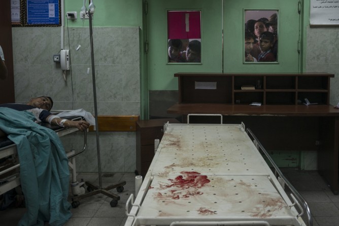 July 24, 2014. Relatives of patients crowd at the windows of an operating room in the hospital in Beit Lahiya, Gaza. Hospitals were often so busy that blood was not wiped from gurneys between patients. (Sergey Ponomarev for The New York Times)