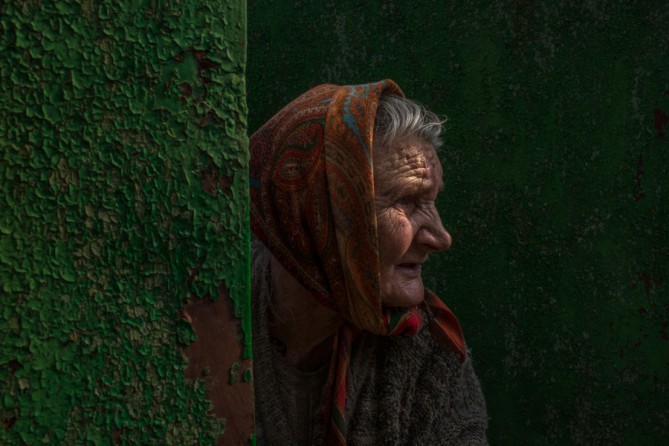 Aug. 1, 2014. A wary Ukrainian, Nadezda Ivanovna, 84, peers through the gate after collecting green apples from a tree near her home, on the outskirts of Slovyansk, a former pro-Russian rebel stronghold back in Ukrainian government control. (Mauricio Lima for The New York Times)