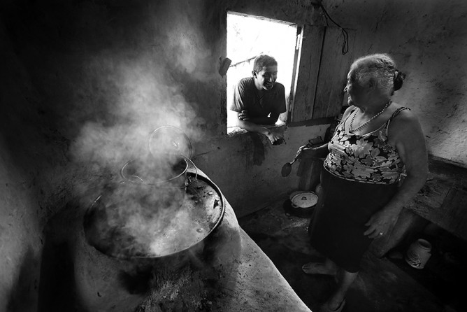 Jose Luis Ramos Castillo, 16, talks with his grandmother Maria de Jesus Rodriguez, 83, through the kitchen window, on Monday, June 30, 2014, as she prepares a pot of frijoles for their family. Castillo had planned to leave for the U.S. the day before with a friend, but the friend backed out because he didn't have the money he wanted to take. The two teens from La Libertad, Honduras are planning another departure date. Castillo hadn't told his grandmother that he planned to leave. (Bob Owen/San Antonio Expre