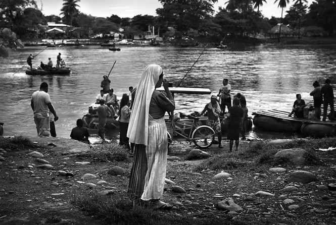 A woman from an evangelical womans group in El Salvador looks across the Suchiate River from the Guatemala side looking for a 'sister' from her group, on the Mexican side, as immigrants and commerce crosses the Suchiate River which is the border between Guatemala and Mexico, in Tecum Uman, Guatemala on Wednesday, July 30, 2014. Ironically, the immigrants would cross a final river - the Rio Grande on the Mexican-Texas border - before crossing into the United States. (Bob Owen/San Antonio Express-News)