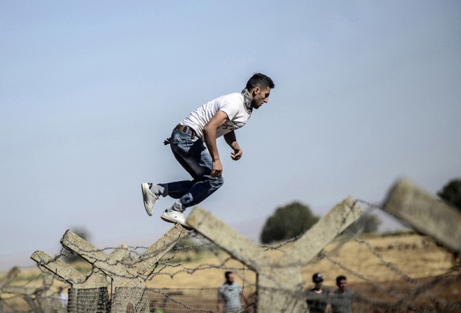 A Kurdish man jumps over the border fence into Syria during a demonstration near the Mursitpinar border crossing at Suruc, Turkey, on September 26, 2014. (Bülent Kılıç/AFP)