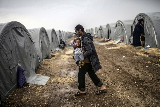 A Kurdish man carries his son during a rainy day at the Rojova Camp in Suruc, Turkey, on October 30, 2014. Rojova houses refugees from Syria fleeing ISIS attacks. (Bülent Kılıç/AFP)