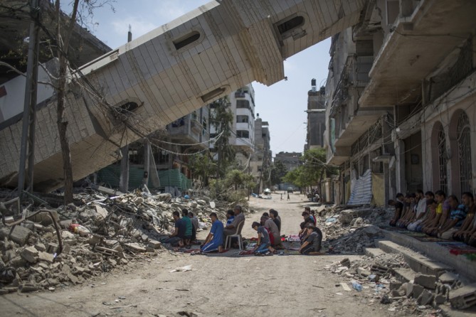 Aug. 15, 2014. Palestinian men pray beneath a toppled minaret at a mosque in Gaza. (Wissam Nassar for The New York Times)