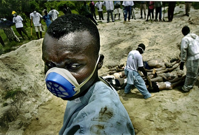 FINAL DUTY: Volunteer Solomon Johnson helps bury 66 bodies in a hurriedly dug mass grave, as peacekeepers' helicopters drone in the distance. (Carolyn Cole)