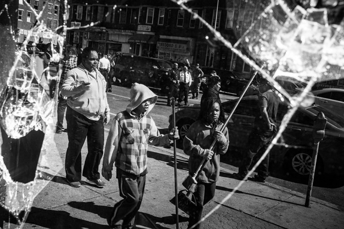 People helping to clean up debris caused by rioting yesterday after the funeral of Freddie Gray are seen in the reflection of a partially destroyed window in Baltimore, Maryland. Gray, 25, was arrested for possessing a switch blade knife April 12 outside the Gilmor Houses housing project on Baltimore's west side. According to his attorney, Gray died a week later in the hospital from a severe spinal cord injury he received while in police custody (Andrew Burton, Getty Images - April 28, 2015).