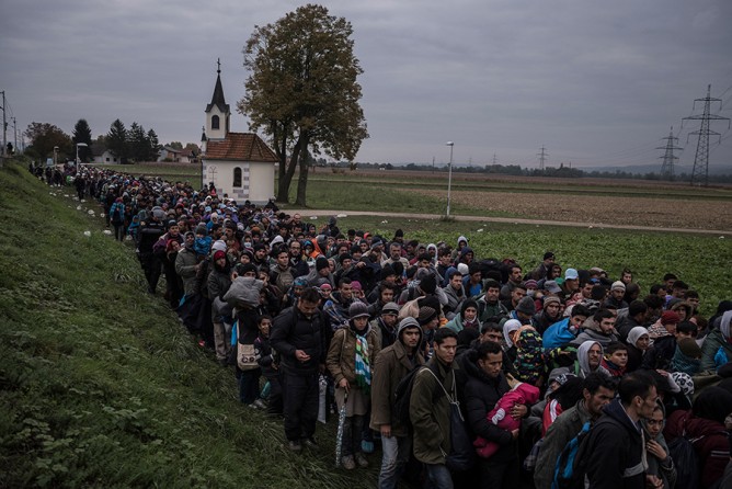 Migrants walking past a church, escorted by Slovenian riot police to a registration camp outside Dobova, Slovenia. The small Balkan nations along the path of the human migration through Europe have seen record numbers of refugees cross their borders, and have been overwhelmed in their ability to manage the human flow (Sergey Ponomarev, The New York Times - October 22, 2015). 