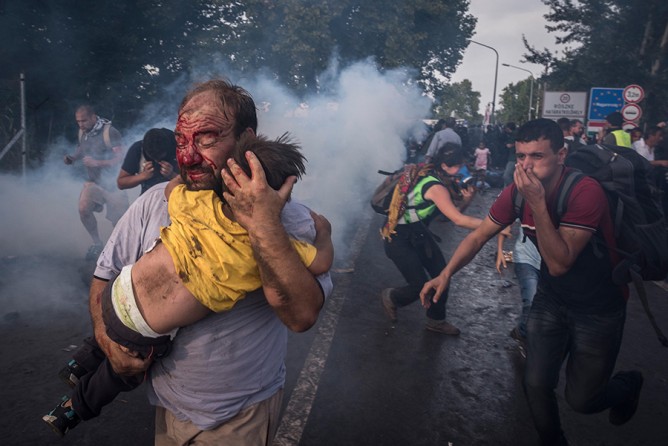 A man tries to shield his child from police beatings and tear gas at the border crossing in Horgos, Serbia. Baton-wielding Hungarian riot police unleashed tear gas and water cannons against hundreds of migrants after they broke through a razor-wire fence and tried to surge into Hungary from Serbia (Sergey Ponomarev, The New York Times​ - September 16, 2015). 