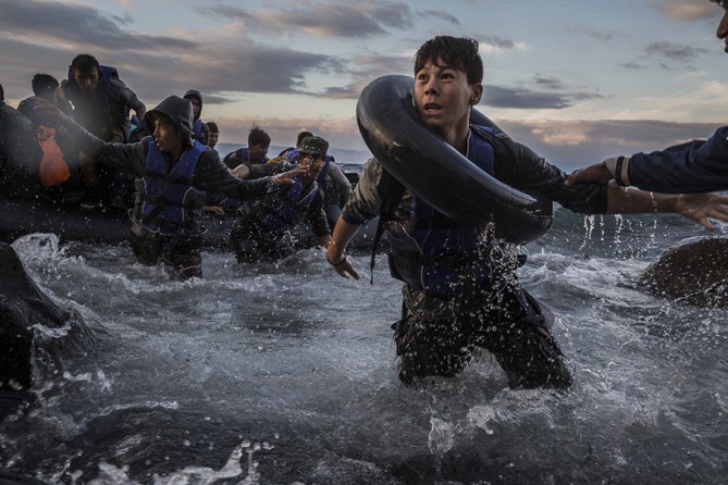 After battling rough seas and high winds from Turkey, migrants arrive by rubber raft on a jagged shoreline of the Greek island of Lesbos. Fearing capsize or puncture, some panicked and jumped into the cold water in desperation to reach land. This young boy made it, unlike hundreds of others (Tyler Hicks, The New York Times - October 1, 2015). 