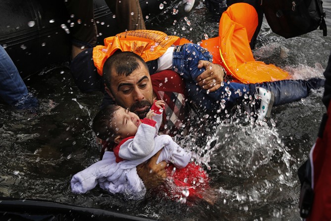 A Syrian refugee holds onto his children as he struggles to walk off a dinghy on the Greek island of Lesbos, after crossing a part of the Aegean Sea from Turkey to Lesbos (Yannis Behrakis, Thomson Reuters - September 24, 2015).