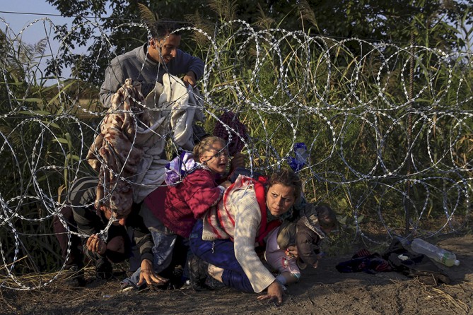Syrian migrants cross under a fence as they enter Hungary at the border with Serbia, near Roszke (Bernadett Szabo, Thomson Reuters - August 27, 2015). 