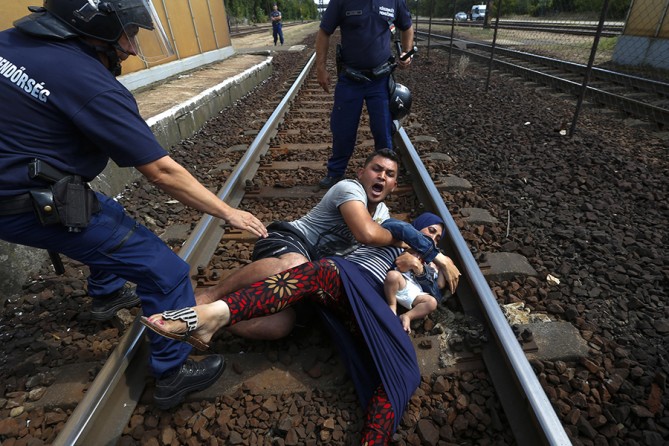 Hungarian policemen stand over a family of immigrants who threw themselves onto the track before they were detained at a railway station in the town of Bicske, Hungary (Laszlo Balogh, Thomson Reuters - September 3, 2015).  