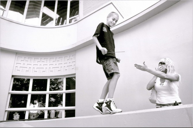 Derek playfully taunts his mother as Cyndie tries to coax him down from a wall outside the UC Davis Medical Center in Sacramento. They are there to admit Derek for cancer surgery the following day. Cyndia, who understands Derek's emotional meltdown before procedures, spends hours getting him in the door of the hospital.