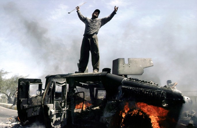 Baghdad - An Iraqi man celebrates atop a burning U.S. Humvee after an explosion that destroyed a building and set four Humvees on fire, killing at least one U.S. soldier.