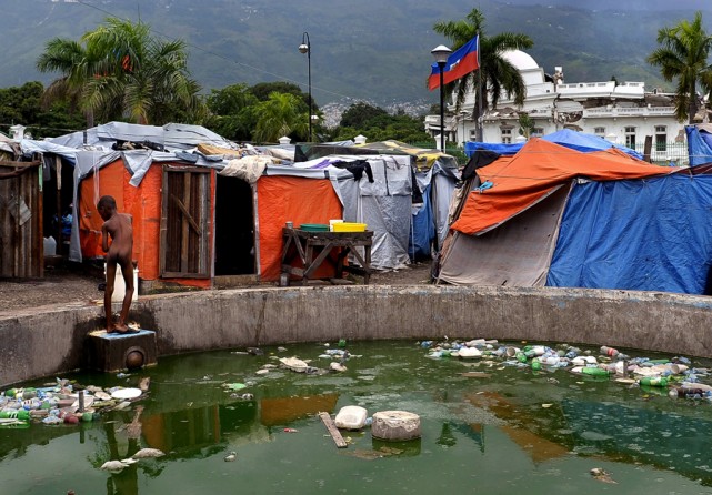 'Squalid Conditions'  Months after the earthquake, a young boy washes in contaminated water at a tent camp near the severely damaged presidential palace looms in the background. The delays in reconstruction reflect bureaucratic red tape in donor nations and the complexity of rebuilding the Western Hemisphere's poorest country, which had little infrastructure, a snarled land-title system and a barely functioning government before the disaster. (Ricky Carioti, The Washington Post - August 22, 2010)