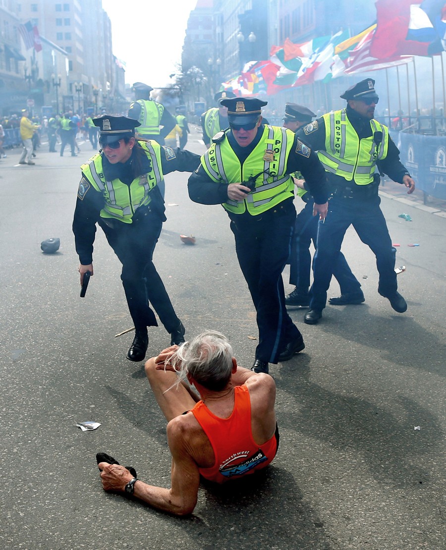 The force of the first bomb blast near the finish line of the Boston Marathon knocks 78-year-old runner Bill Iffrig to the ground. As the second bomb explodes, Boston Police Officers Rachel McGuire, Kevin McGill and Javier Pagan react in the initial confusion. (Photo by John Tlumacki, April 19, 2013)