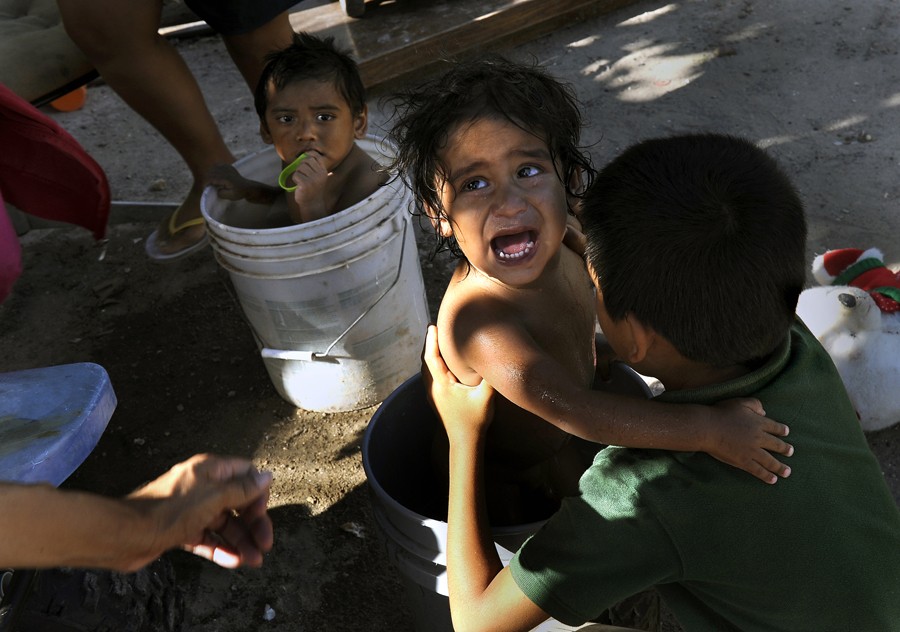 McAllen, Tex.: Christopher Vasquez, 5, hoists his 1-year-old brother Joel from a bucket where he was being given a bath. Brother Julio, 2, at left, seems less anxious. Nutrition educators asked their mother, Francesca Vasquez, to participate in a nutrition education program designed to combat growing obesity in Hidalgo residents. She agreed to meet with educators at her home. (November 10, 2013)