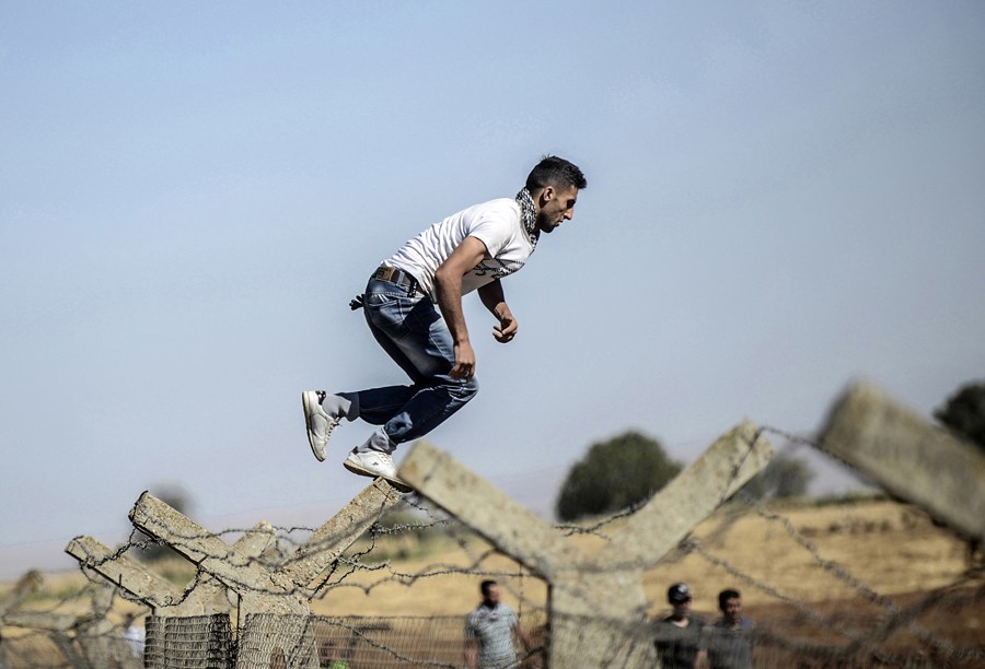 A Kurdish man jumps over the border fence into Syria during a demonstration near the Mursitpinar border crossing at Suruc, Turkey, on September 26, 2014. (Bülent Kılıç/AFP)