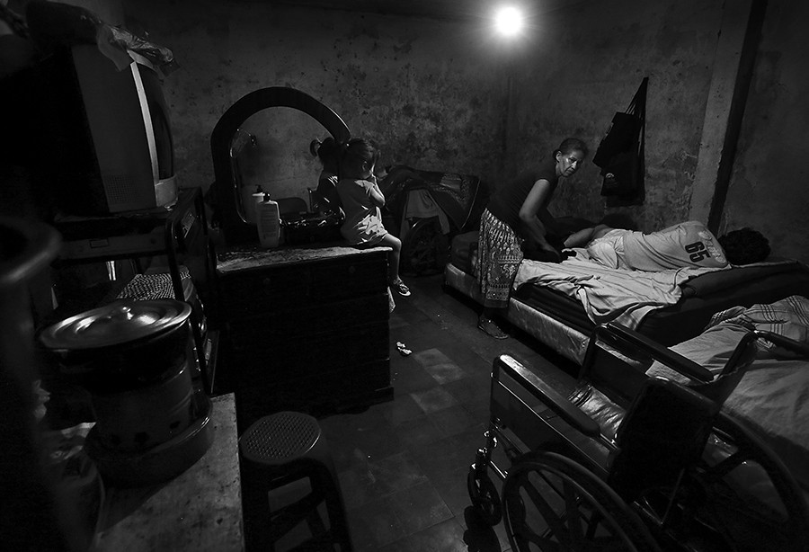 Gloria Nunez, 49, changes the diapers for her injured son Allan Cruz, 22, on Monday, June 30, 2014. Cruz was hit by a vehicle in Celaya, Mexico, while heading to Houston, to look for work back in 2011. The family of six live in a one room apartment in Barrio El Pedregalito in Tegucigalpa, Honduras. Nunez's kitchen consists of a portable gas burning-one-pot stove, at left. (Bob Owen/San Antonio Express-News)