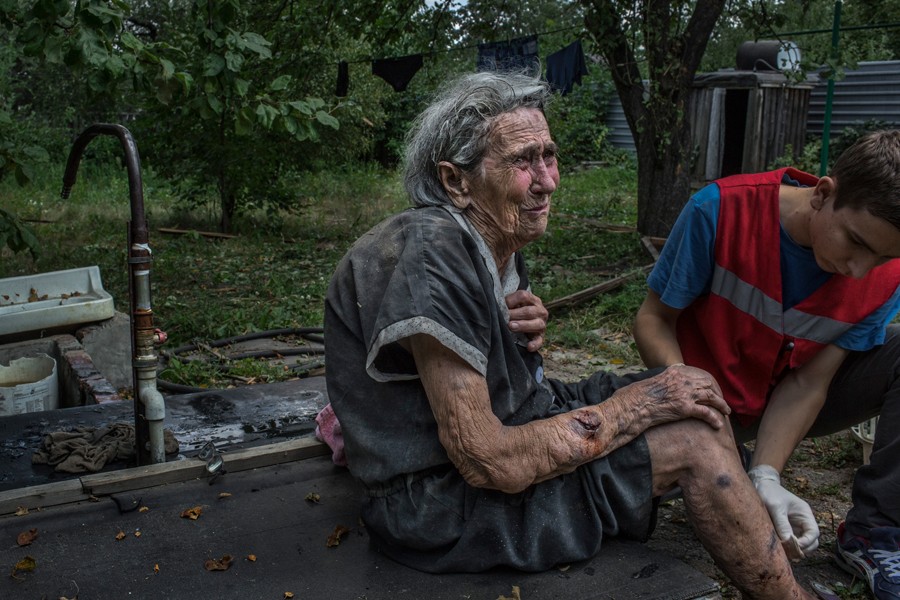 Aug. 10, 2014. Lisa Soroka, 80, grandmother of Roman Pronyakin, 37, who died while watching TV inside his bedroom during a rocket attack, cries as she receives first aid from a doctor after being injured by heavy shelling near the Donetsk airport. (Mauricio Lima for The New York Times)