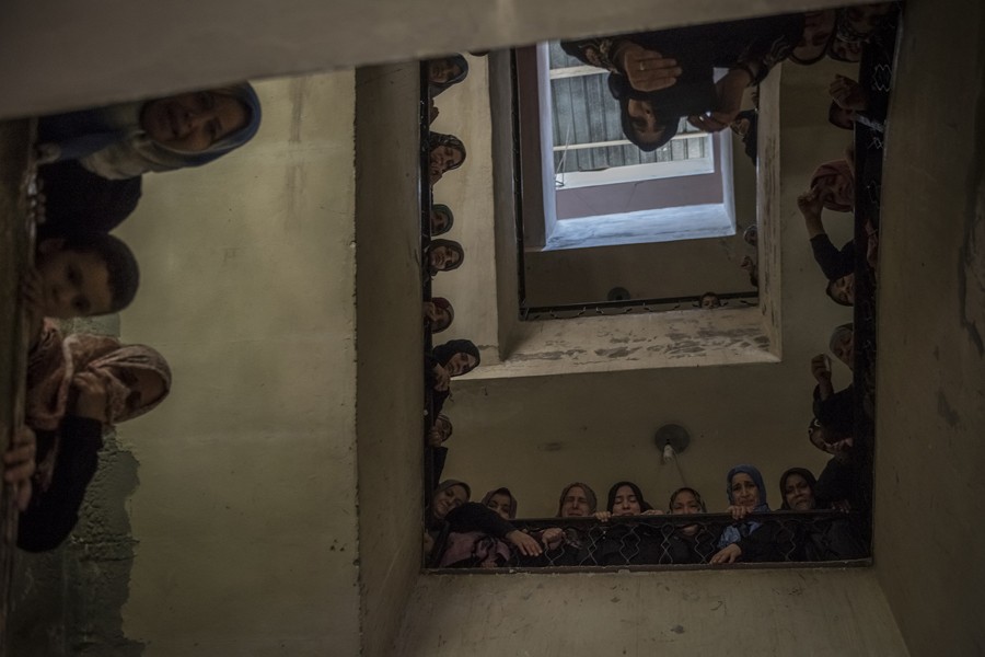 July 22, 2014. Barred from the proceedings, women peer from a stairwell for a glimpse of the funeral of a 27-year-old Islamic Brigades fighter in an extended family home in Deir al-Balah. (Sergey Ponomarev for The New York Times)