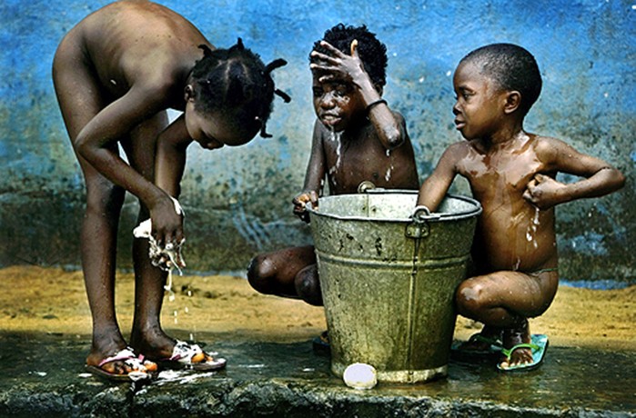 FEW COMFORTS: Ester Burges, 6, Sarrah Barbar, 7, and Sabay Ndebe, 5, bathe from a bucket of cold water at the Hannah B. Williams center. the number of orphans in war-devastated Liberia now tops 10,000, officials say. (Carolyn Cole)