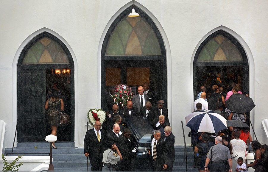 Pallbearers exit Emanuel AME Church carrying the casket of Cynthia Hurd while mourners for Susie Jackson and her nephew Tywanza Sanders file inside the church for their funerals in the lightning and heavy rain. The three were among nine worshippers to die in a mass shooting at the church on June 17. A procession of caskets and funerals filled the church for days (Grace Beahm, The Post and Courier - June 27, 2015).
