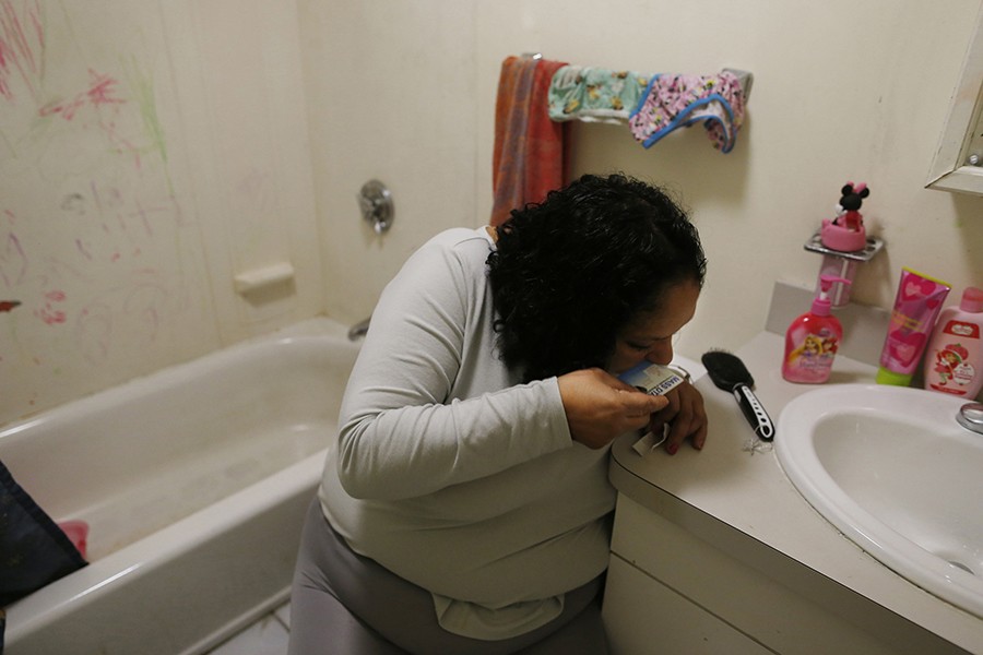 With the bathroom door locked to keep her daughters out, Raquel leans over and snorts heroin inside her apartment. Moments earlier, Estrella had tried to block her mother's way into the bathroom, and now the girls are crying outside of the door as she gets high (Jessica Rinaldi, The Boston Globe).