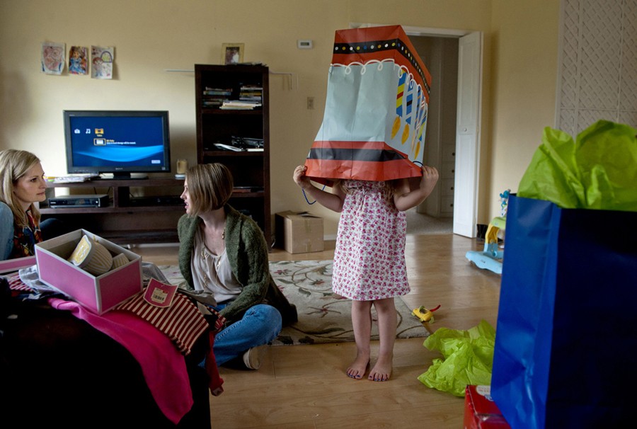 As babysitter Brandy Stanley, 37, center, chats with Frankie Young, left, Eva Winkler peeks into a bag after celebrating her fifth birthday.  (May 16, 2012)