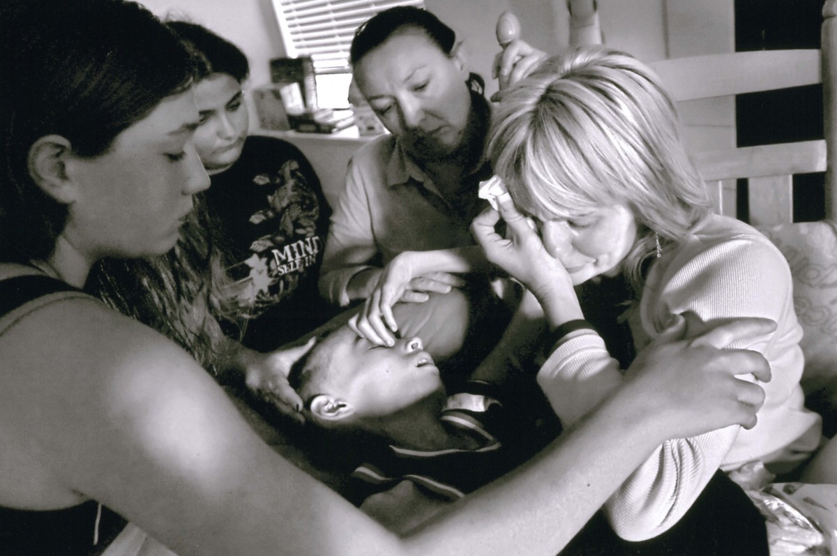 Cyndie rocks her dying son as the song, "Because We Believe," plays on a cd. She sings along with Andrea Bocelli in a whispery voice. "Once in every life/There comes a time/We walk out all alone/And into the light..." From left, family friends Ashley Berger, Amy Morgan and Kelly Whysong offer comfort as Cyndie tells Derek, "It's OK, baby. I love you, little man. I love you, brave boy. I love you. I love you." Derek died soon after in his mother's arms on May 10, 2006.