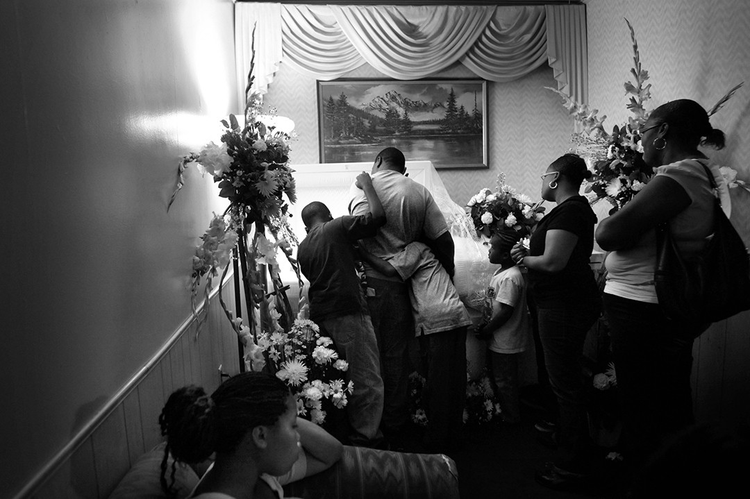 Seventeen year-old Edwin Cobbin was lifting weights in the front yard of his house in Hawthorne when dark SUV pulled up. Two men got out, searched his pockets and asked him what gang he belonged to. Edwin told them he wasn’t in a gang, but the men shot him and drove away. ’I am not okay,’ said his grandmother, Helen Glee. ‘None of us are.’  Loved ones mourn over Edwin’s casket at a public viewing.  (Barbara Davidson, Los Angeles Times)