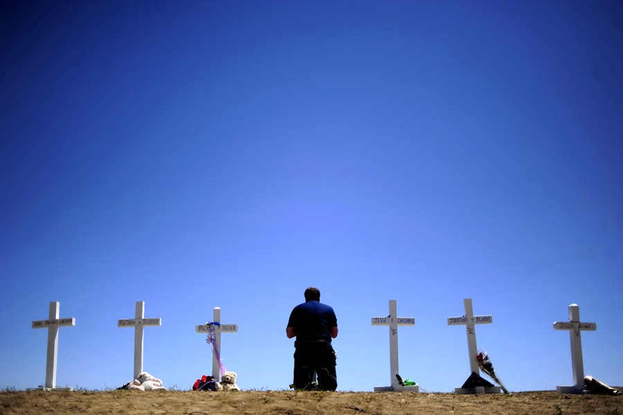 Travis Hirko kneels at the cross of Alex Sullivan at a memorial for the victims of the Aurora Theater Shooting at the intersection of Sable Boulevard and Centerpoint Drive on Sunday, July 22, 2012. (Aaron Ontiveroz - July 23, 2012)