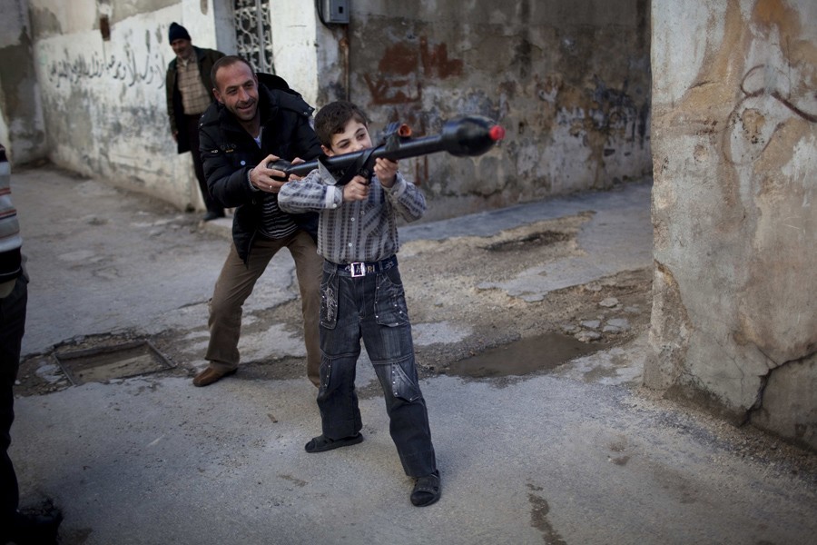 A man teaches Bilal, 11, how to use a toy rocket propelled grenade in Idlib, northern Syria, March 4, 2012. (Rodrigo Abd, Associated Press - March 4, 2012)