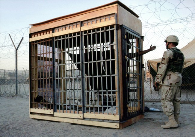 Baghdad - A detainee in a solitary confinement cage talks with a military policeman at Abu Ghraib prison. U.S. soldiers said the prisoner had frequently fought with other inmates. 